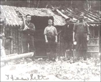 photo of four men standing outside of a log cabin