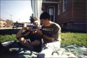 Two persons sitting on a blanket, one is playing a guitar
