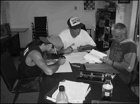 Three men sitting around a table doing some work.