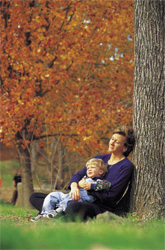 A woman sitting by a tree holding her son
