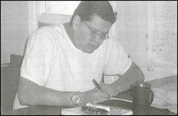 photo of a male person sitting at a desk and writing in a book