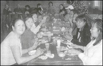 photo of several people sitting on both sides of a long table and eating a meal